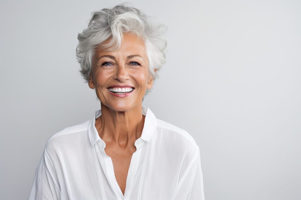 Woman with white hair smiling in front of off-white background