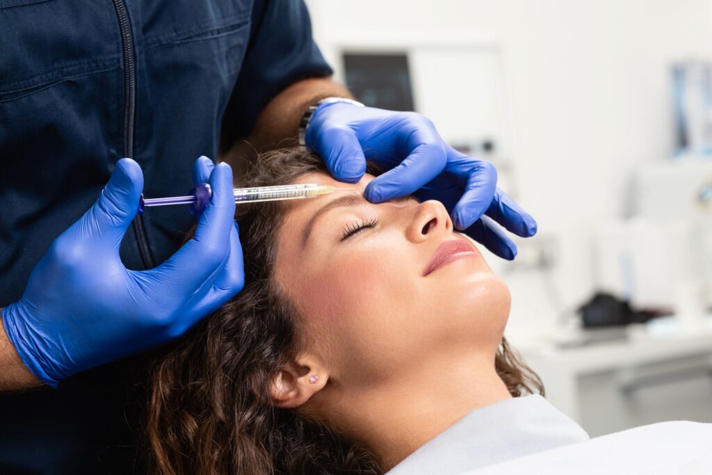 Woman with dark hair receiving botox injections in forehead by professional in blue gloves